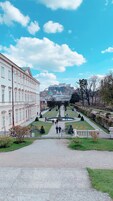 Un jardín formal con una fuente central, senderos y un edificio grande de arquitectura clásica al fondo.