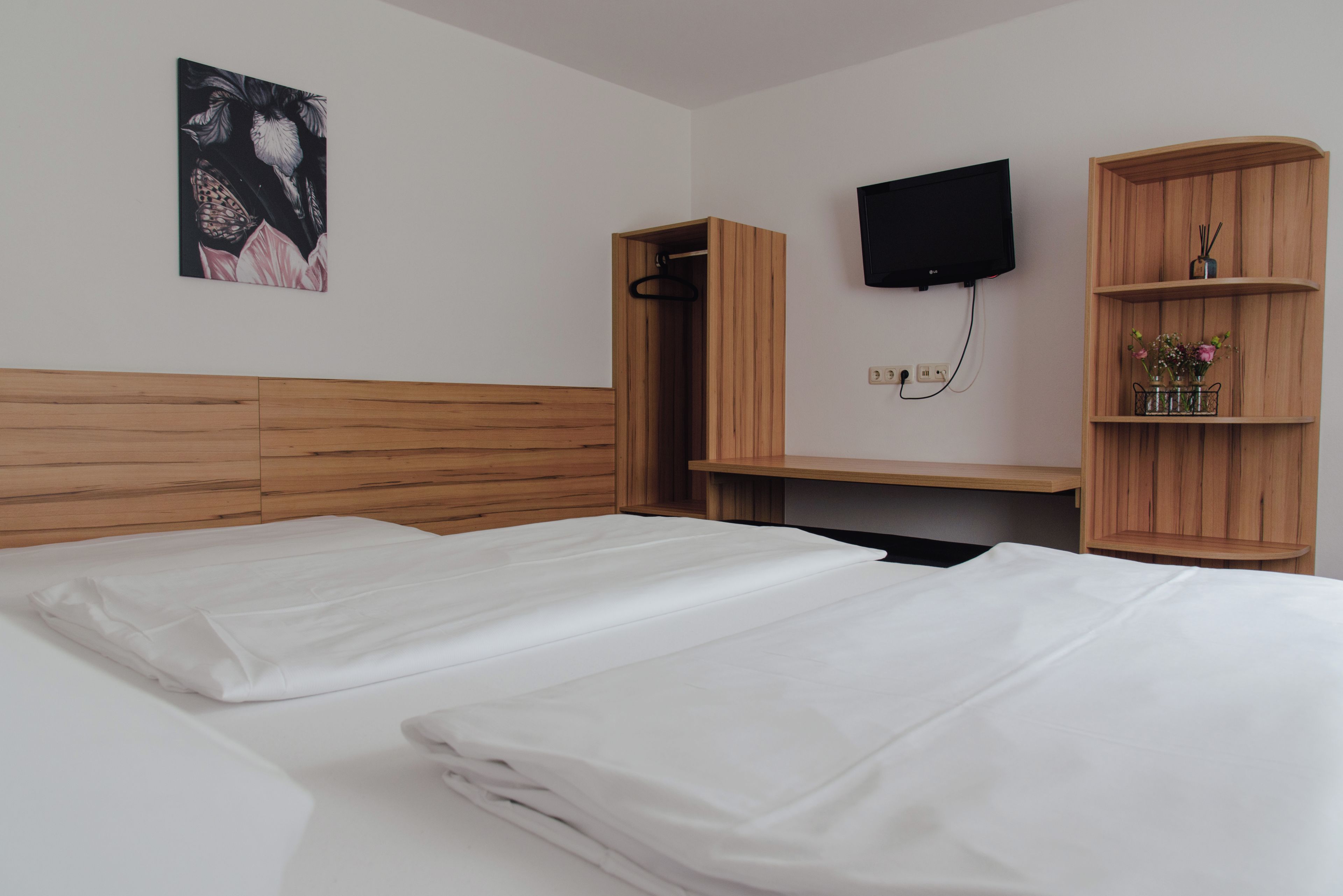 Een hotelkamer met twee bedden, een houten hoofdbord, een flatscreen televisie aan de muur en een houten plank met decoratieve objecten.