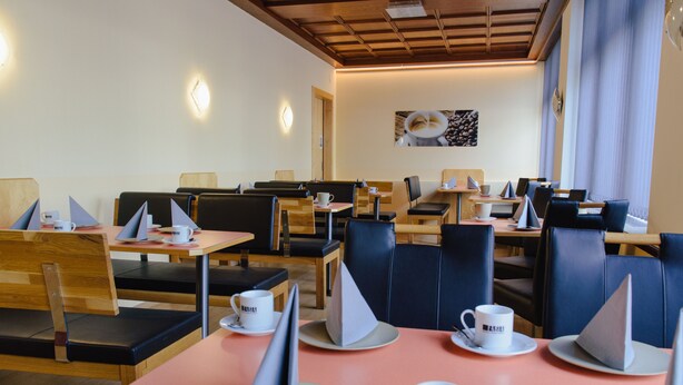 A modern cafe with wooden tables and black leather chairs, featuring a clean and minimalist design. - Hotel Drei Kreuz (Salzburg)