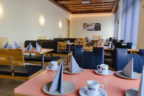 A modern cafe with wooden tables and black leather chairs, featuring a clean and minimalist design. - Hotel Drei Kreuz (Salzburg)