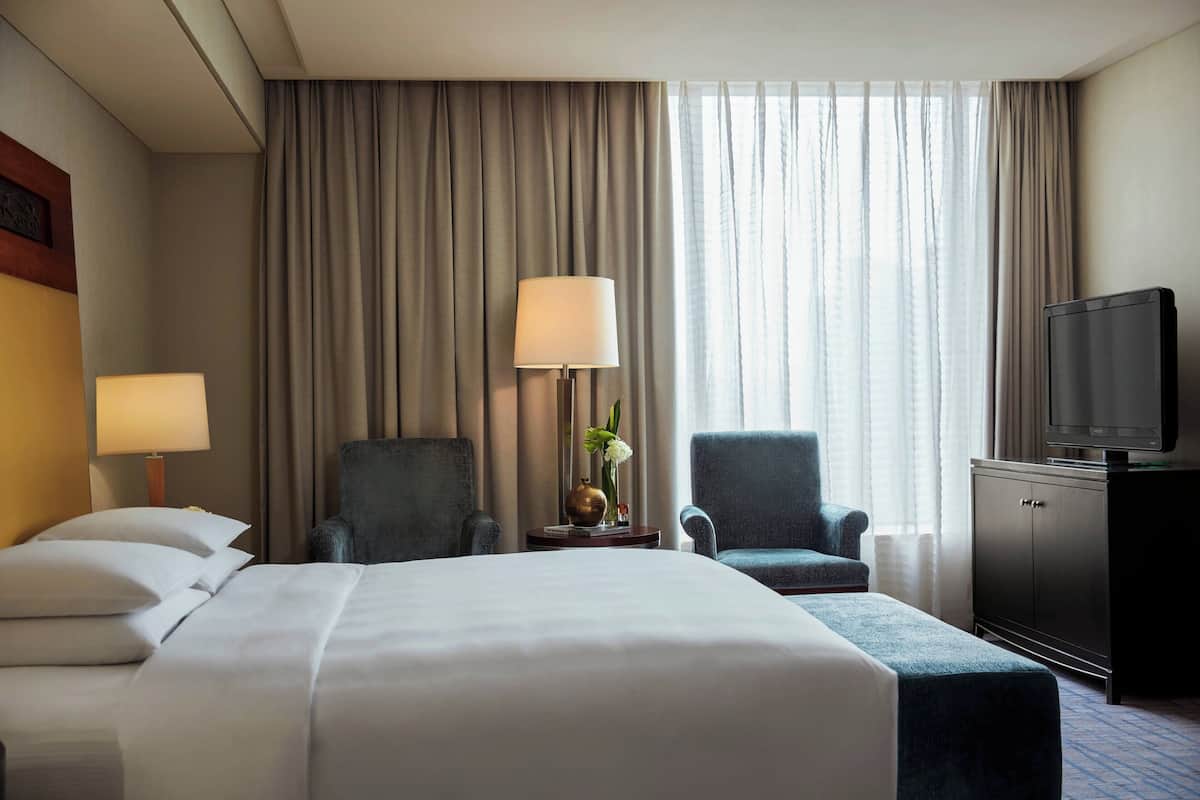 A hotel room with a large bed, two armchairs, a television, and a vase with flowers.