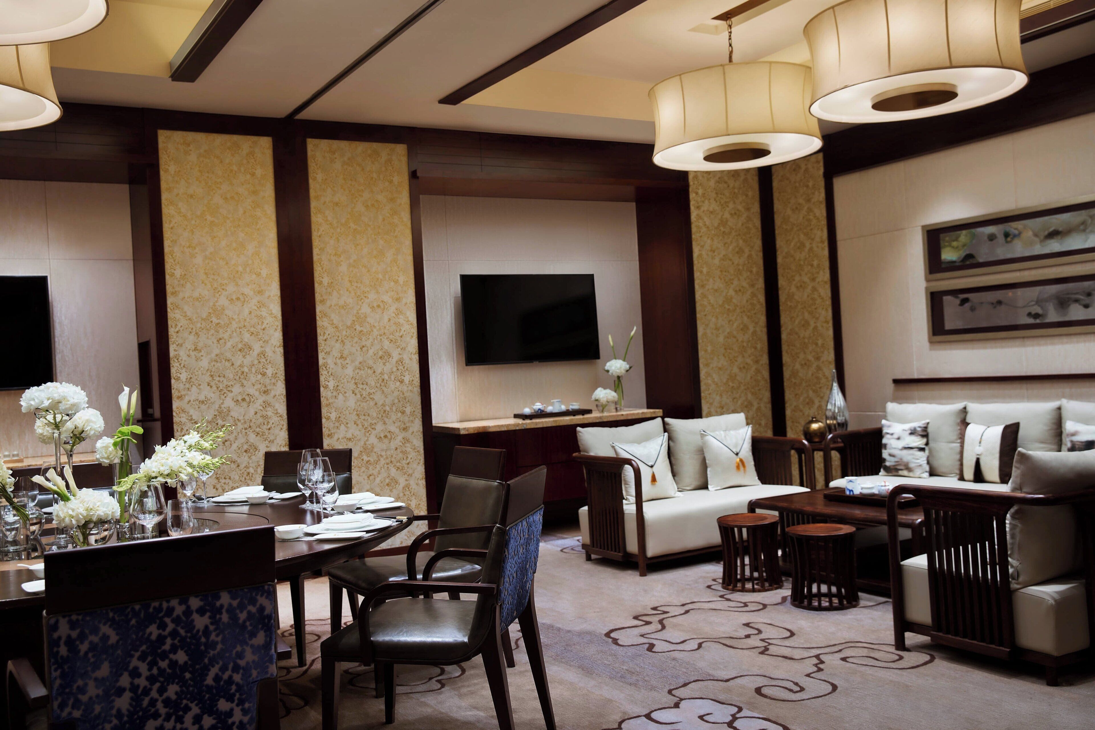 A modern hotel lobby with a dining area, sofas, and a flat-screen TV.