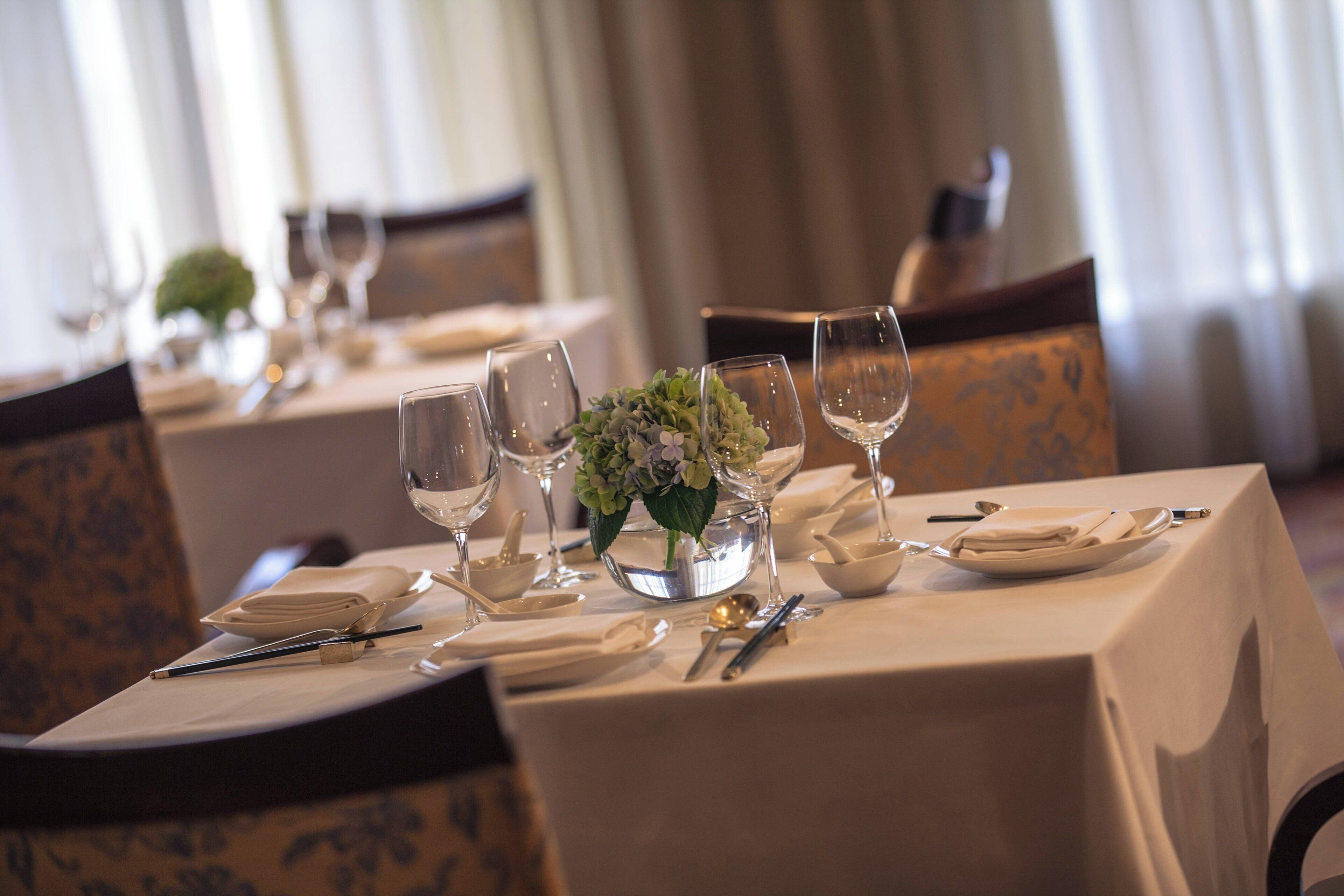 A dining table set with plates, cutlery, and wine glasses, with a centerpiece of flowers.