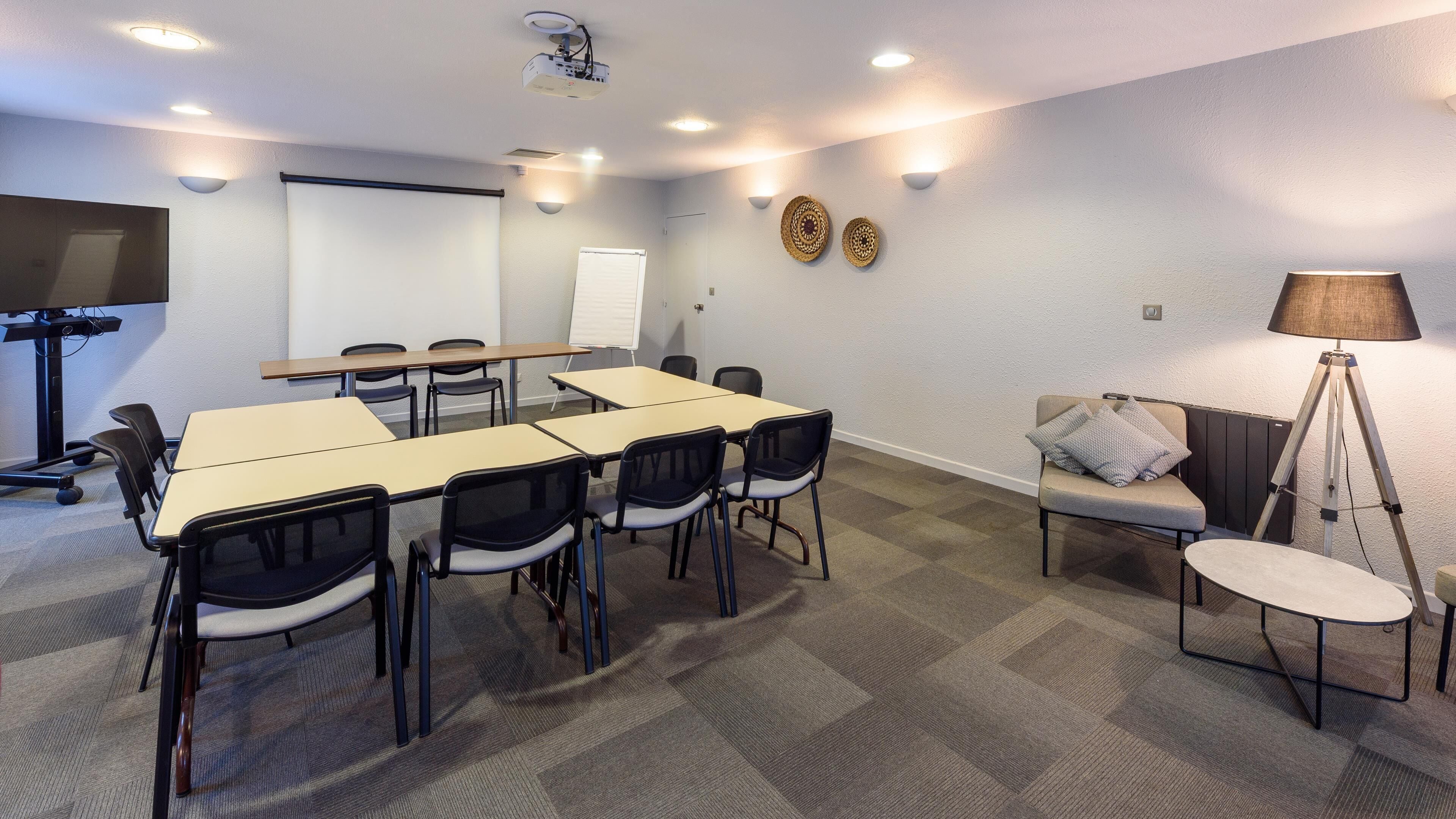 A conference room with a long table, chairs, a projector, a whiteboard, and a sofa with a lamp.