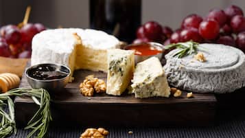 A variety of cheeses, grapes, walnuts, and a bottle on a wooden board.