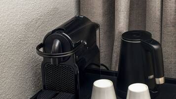 De minibar in een hotelkamer, met een koffiezetapparaat, twee witte bekers en diverse snacks en drankjes.