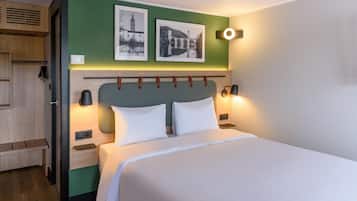 A hotel room with a bed, two wall-mounted lamps, a green accent wall, and two framed pictures.