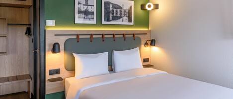 Quarto de hotel com uma cama, duas luminárias fixadas na parede, uma parede verde decorativa e duas imagens emolduradas.