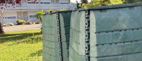 Two large green storage bins in a grassy area with a building in the background.
