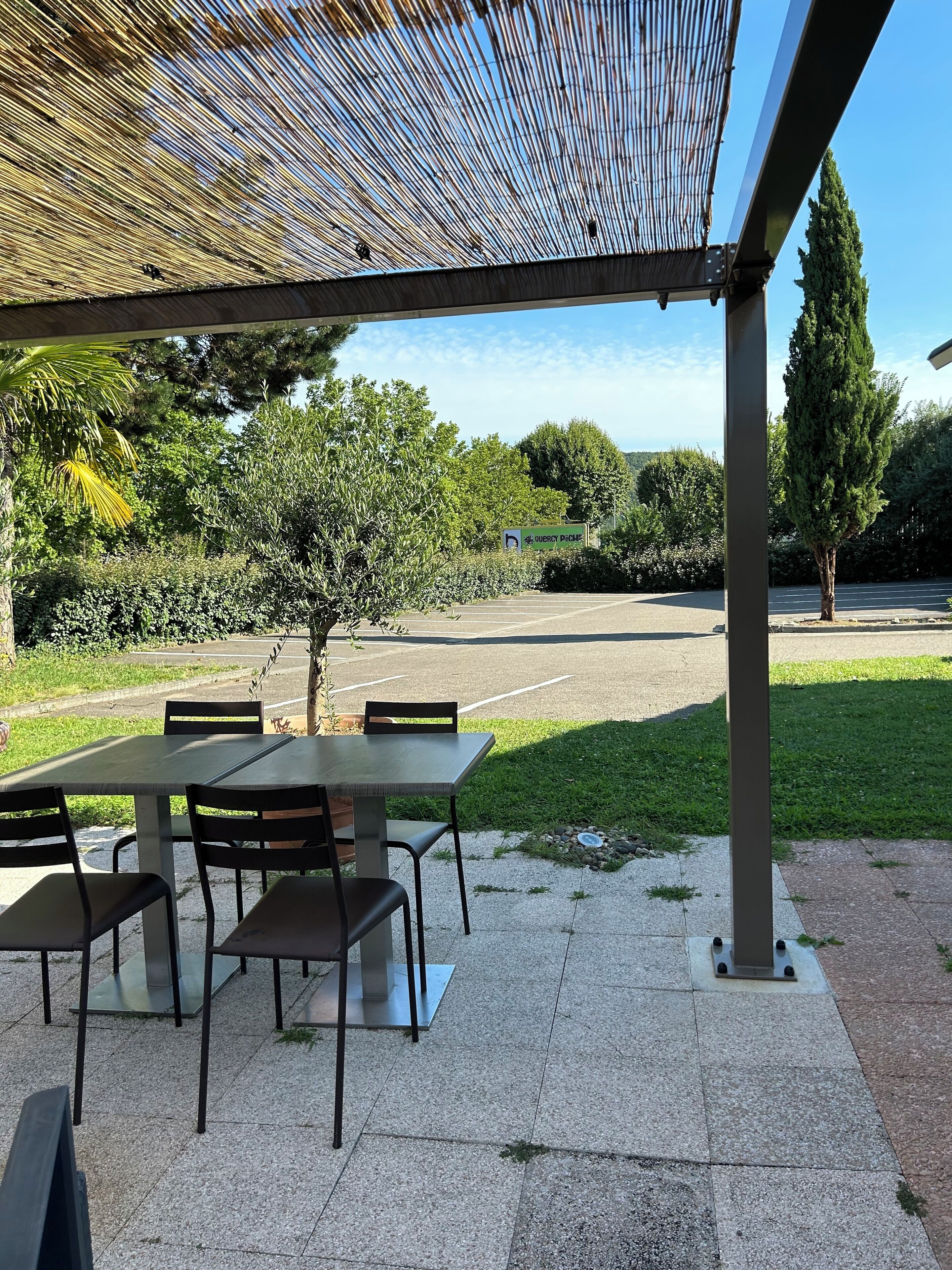 Un patio al aire libre con una zona de estar cubierta, un árbol pequeño y un estacionamiento al fondo.