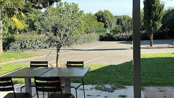 Un patio al aire libre con una zona de estar cubierta, un árbol pequeño y un estacionamiento al fondo.