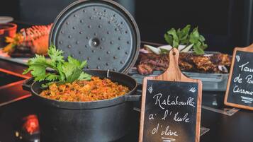 A restaurant setting with a black pot of ratatouille, a wooden board with a chalkboard menu, and a tray of food.
