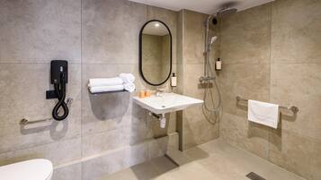 Une salle de bain moderne équipée de toilettes, d’un lavabo, d’un miroir, d’un porte-serviettes et d’une douche.