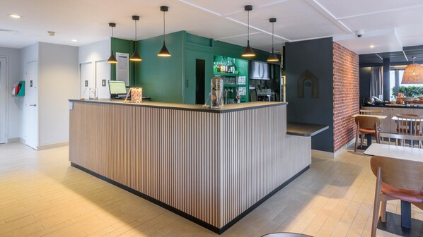 A modern reception area with a green accent wall, a wooden reception desk, and pendant lighting. - Campanile NATURE - Cahors (Cahors)