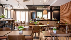 A modern restaurant with wooden tables and chairs, a bar area, and potted plants.