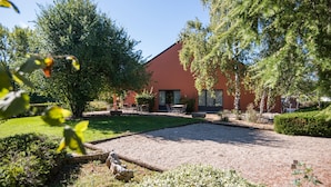 Ein Gebäude mit roter Fassade, umgeben von einem gepflegten Garten mit verschiedenen Pflanzen und einem Kiesweg.