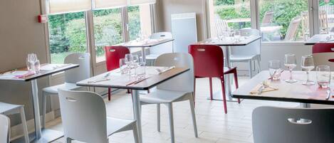 A restaurant with tables and chairs, some with red chairs and others with white chairs.