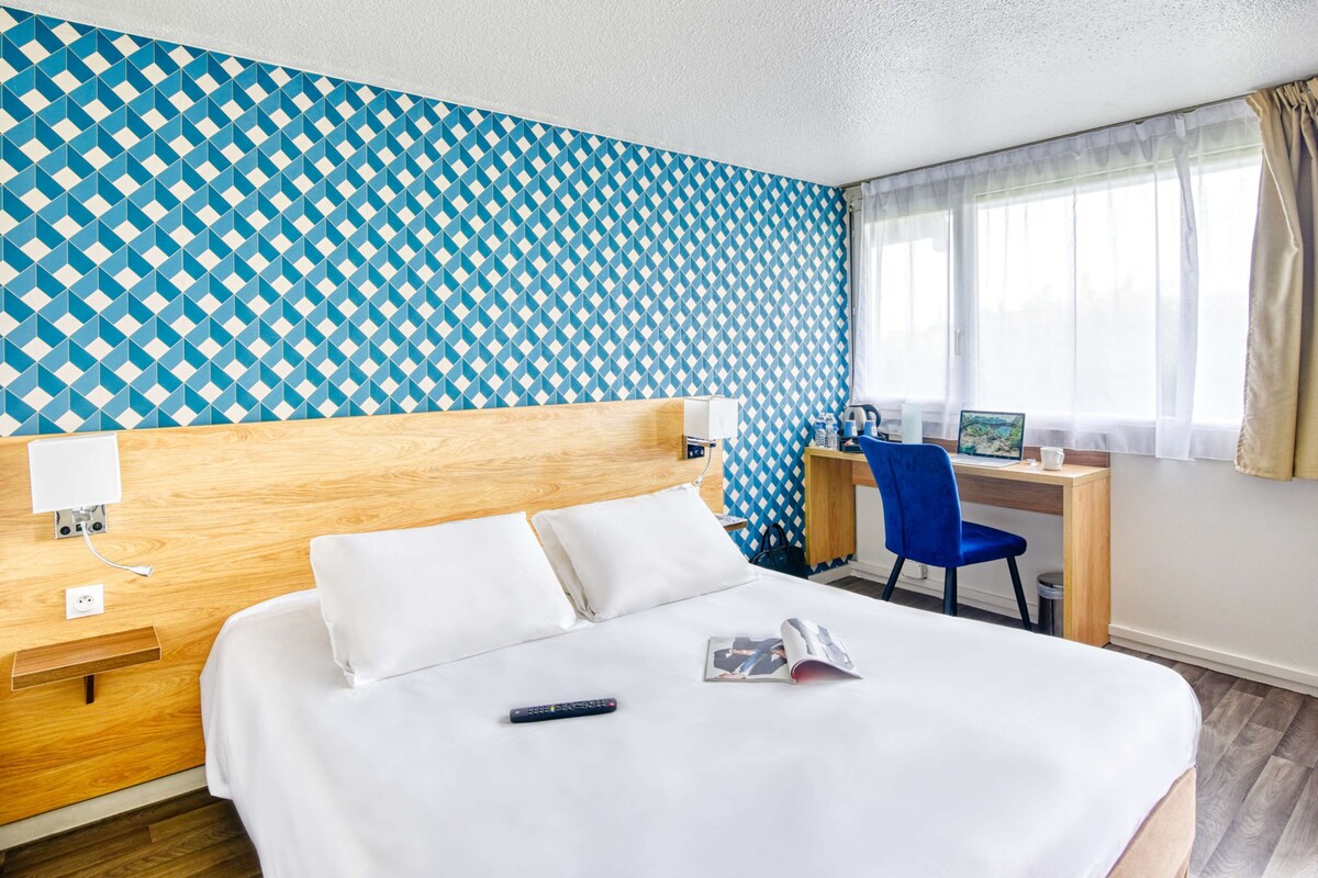 Een hotelkamer met een bed, een bureau, een stoel en een raam met gordijnen.