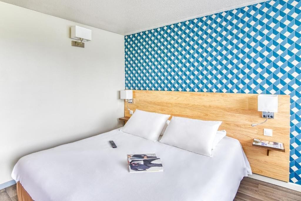 Una habitación de hotel con una cama grande, ropa de cama blanca, un papel tapiz azul y blanco y un cabecero de madera.