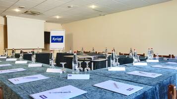 Sala de conferências com uma mesa comprida, porta-nomes, garrafas de água e uma tela de projetor exibindo 'Kyriad Hotel'.