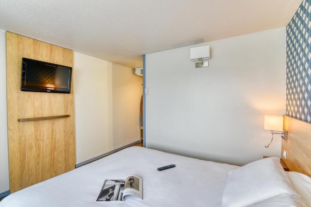Habitación de hotel con una cama, un televisor montado en un panel de madera, un aire acondicionado de pared y un papel tapiz estampado.