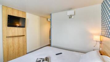 Habitación de hotel con una cama, un televisor montado en un panel de madera, un aire acondicionado de pared y un papel tapiz estampado.