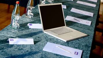 A laptop on a table with name tags, a glass, and a pen.