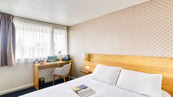 A hotel room with a bed, a desk, a chair, and a window with curtains.
