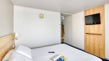 Une chambre d’hôtel avec un lit, un téléviseur fixé au mur, une armoire et une lampe.
