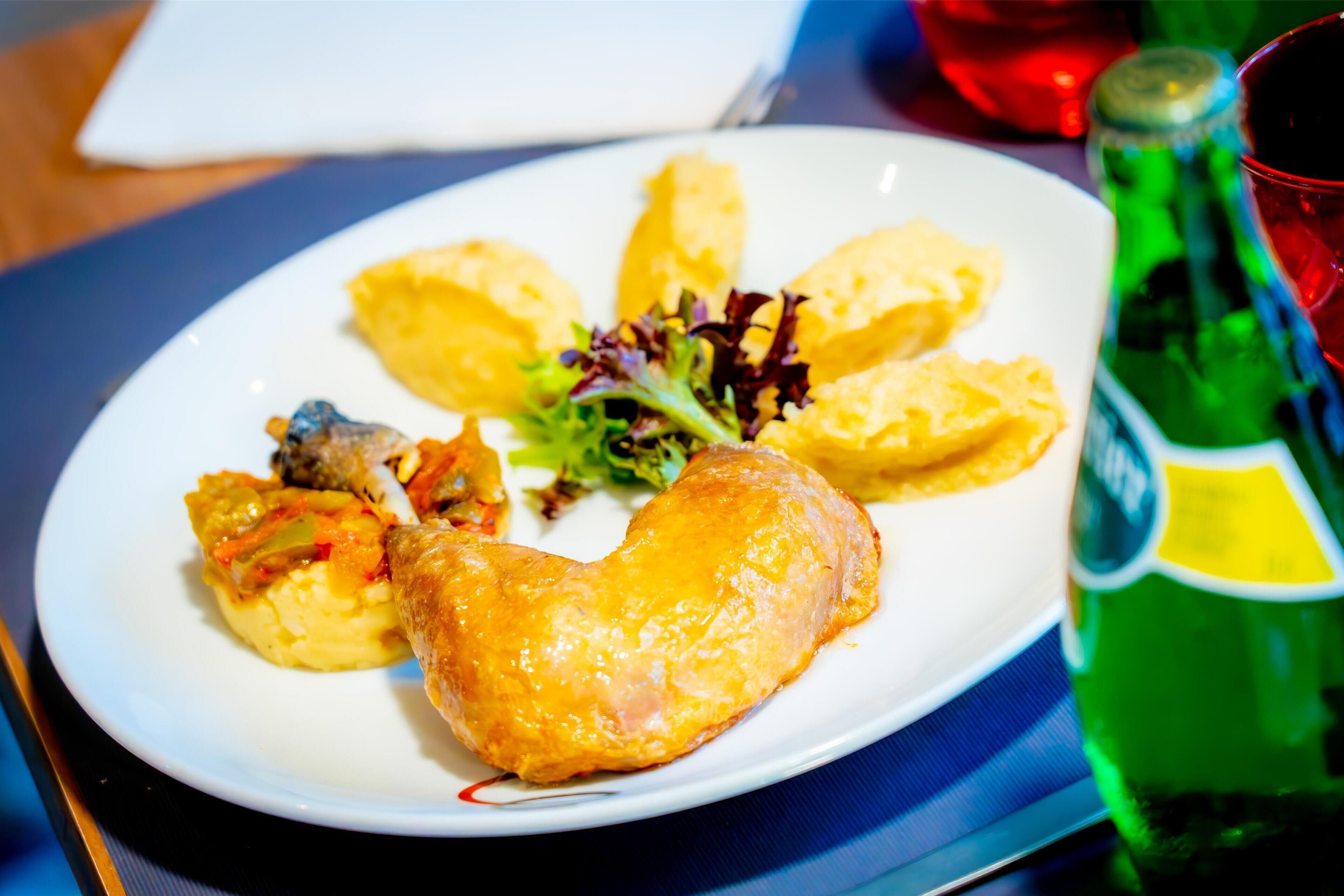 Un plato de comida con una botella de bebida verde y un vaso rojo.