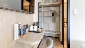 Een compacte hotelkamer met kitchenette, spiegel, een klein zithoekje en een deur naar de badkamer.