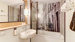 Een moderne badkamer met een grote spiegel, een wastafel, een bad en uitzicht op een straat door een glazen deur.