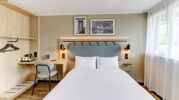 Une chambre d’hôtel comprenant un lit, un bureau, une chaise, une armoire et deux tableaux encadrés accrochés au mur.