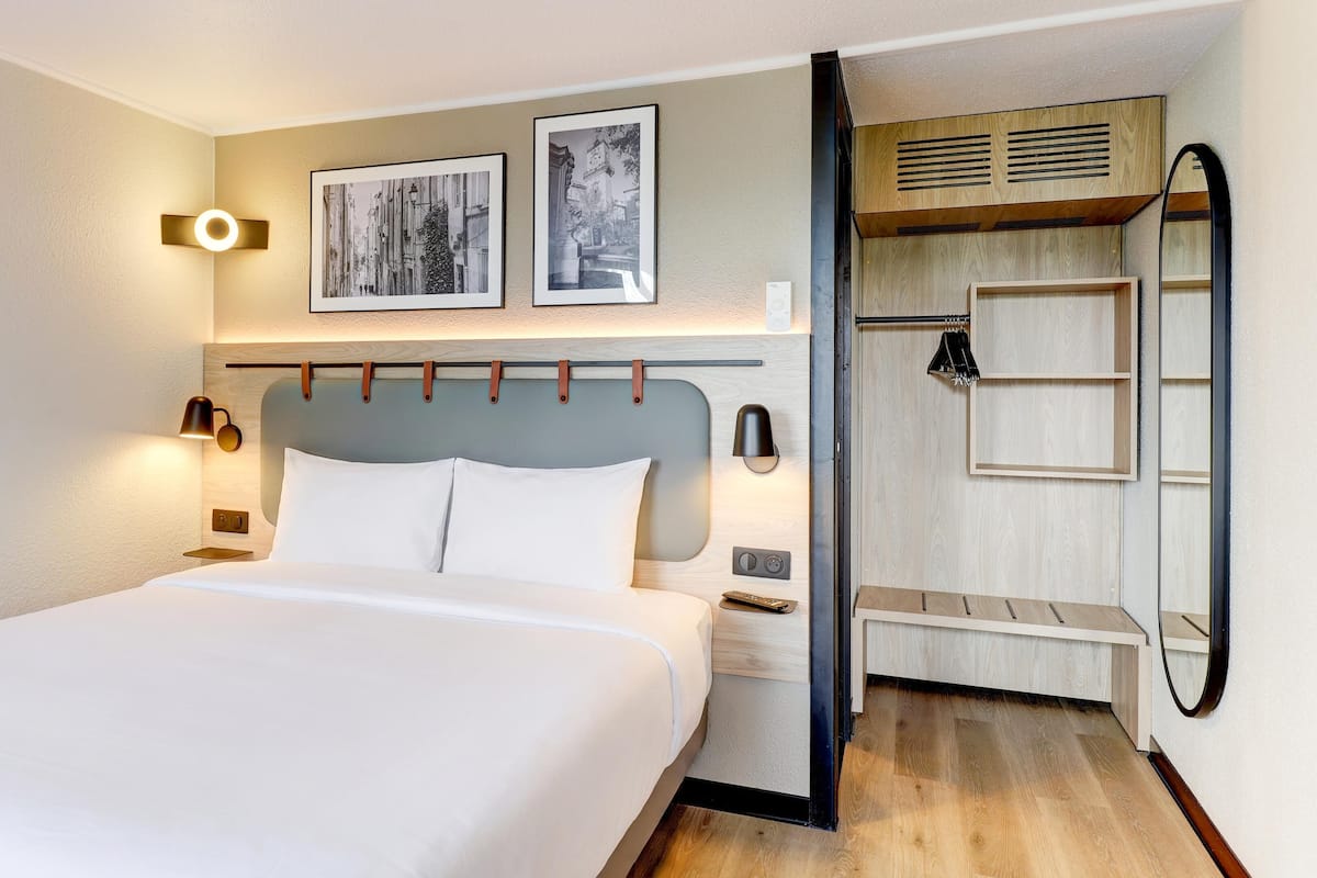 Ein Hotelzimmer mit Bett, Nachttischen, einem Kleiderschrank und einem Spiegel.