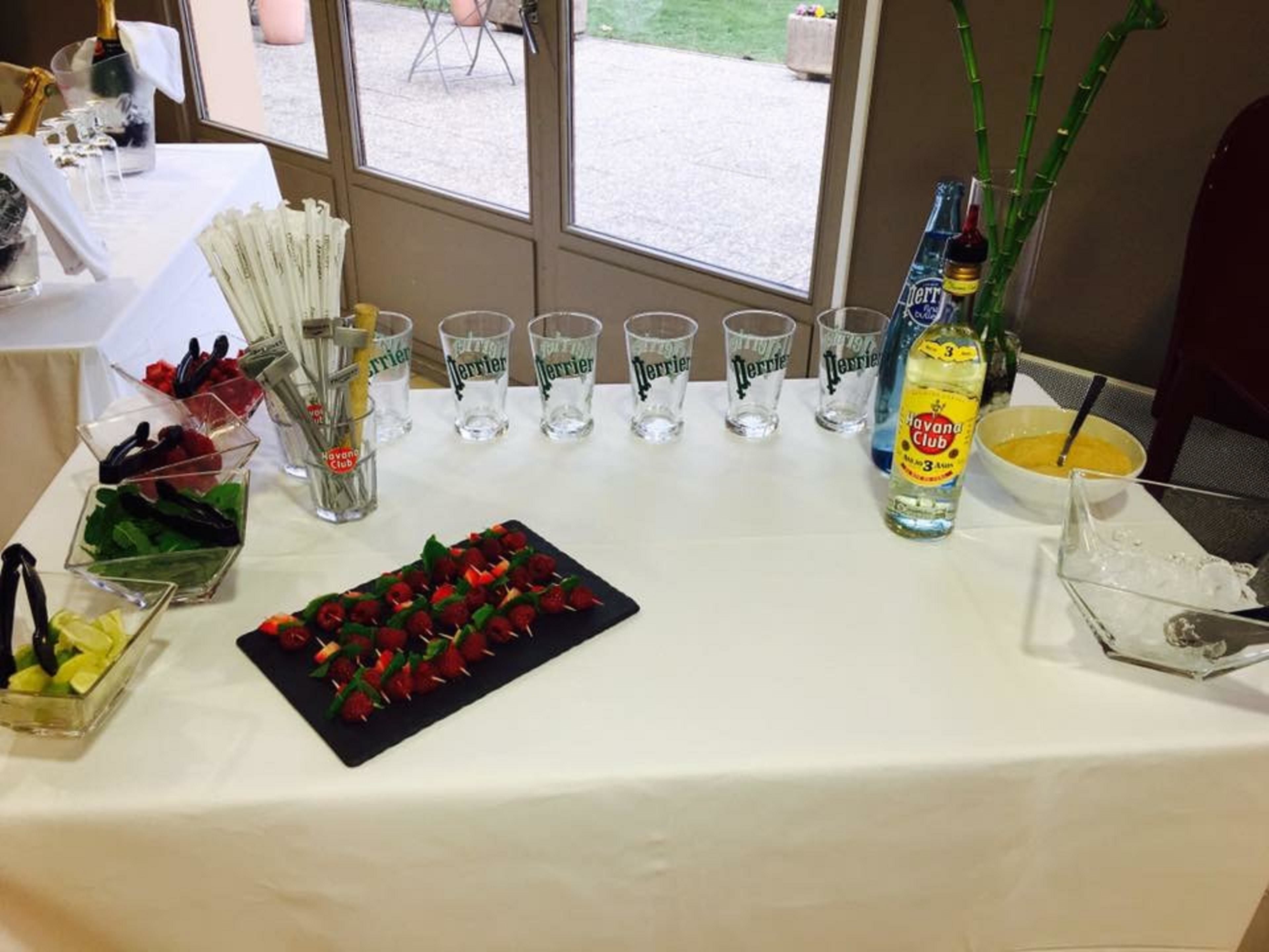 A table with a variety of food items, including a plate of strawberries, a bowl of soup, and several glasses of Perrier water.