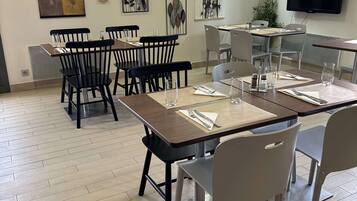 A dining area with wooden tables and chairs, framed artwork on the walls, and a clock.