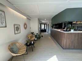 A hotel lobby with a reception desk, seating area with chairs, potted plants, and framed artwork on the walls.