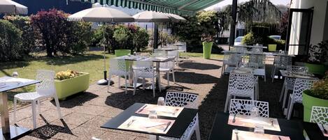 Une terrasse extérieure avec des tables et des chaises, des parasols et des plantes en pot.