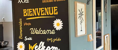 A wall with a blackboard displaying multilingual welcome messages and flower decorations.