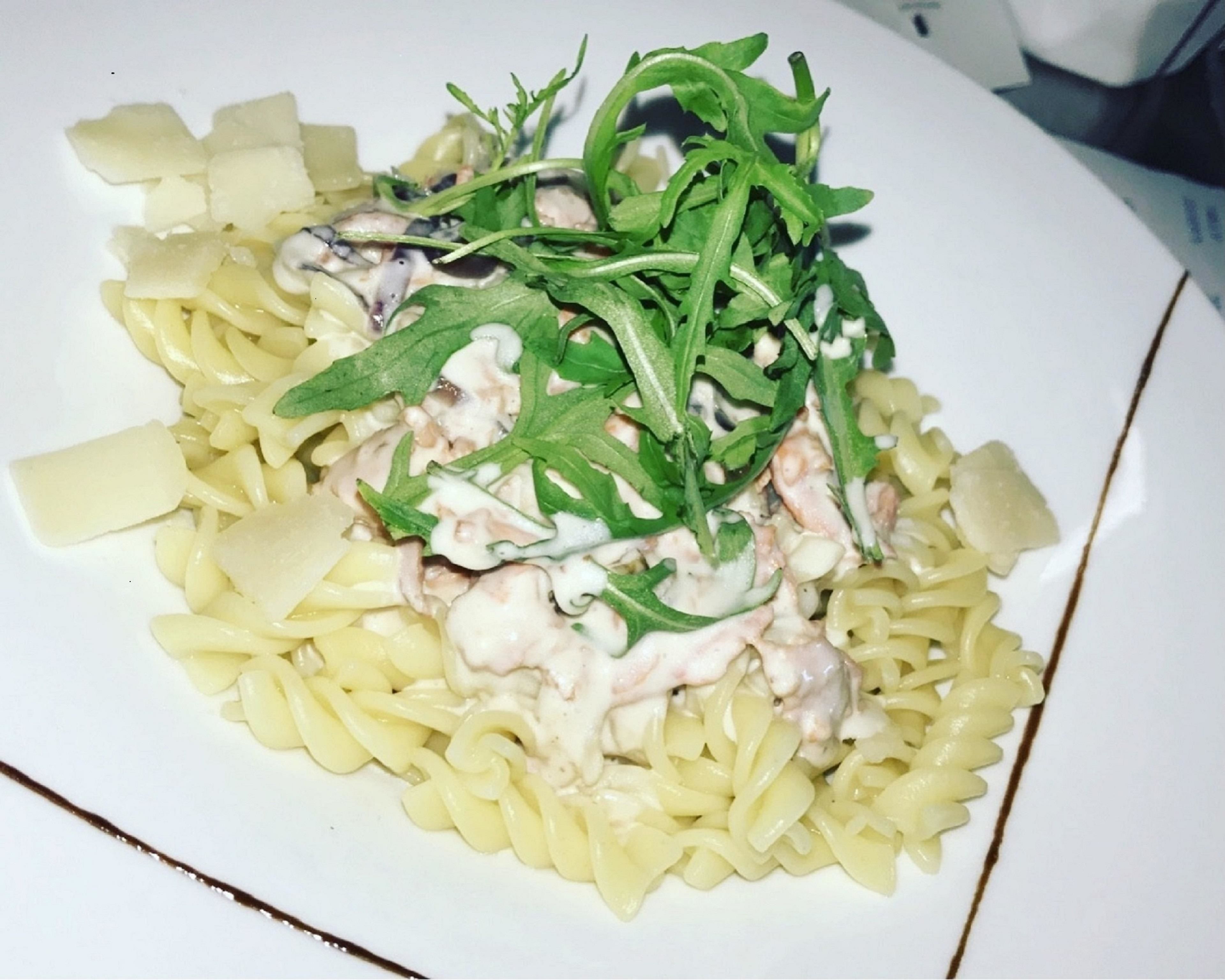 Une assiette de pâtes nappées d’une sauce crémeuse, garnie de roquette et de morceaux de poulet.