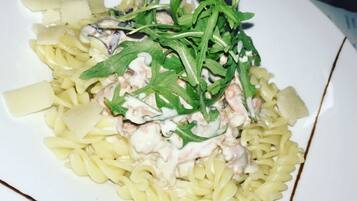 Een bord pasta met een romige saus, afgetopt met rucola en stukjes kip.