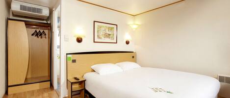 A hotel room with a bed, a wardrobe, a nightstand, a lamp, and a picture on the wall.