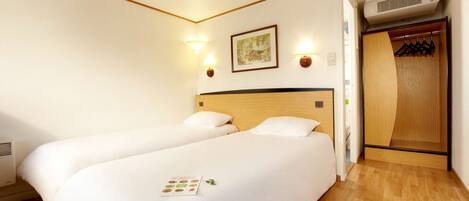 A hotel room with two beds, a wooden wardrobe, and a wall-mounted air conditioner.