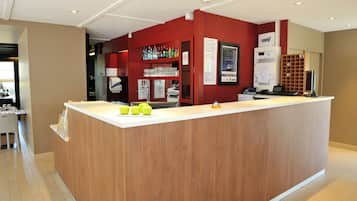 A reception desk with a wooden counter, a red wall, and a glass display case with bottles.