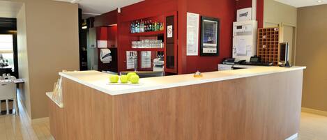 A reception desk with a wooden counter, a red wall, and a glass display case with bottles.