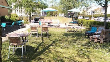 An outdoor seating area with tables and chairs, umbrellas, and a grassy lawn.