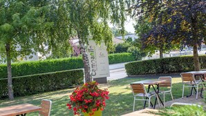Un área de estar al aire libre con mesas y sillas, un letrero que dice 'Campanile Hotel Restaurant' y una planta grande en maceta con flores rojas.