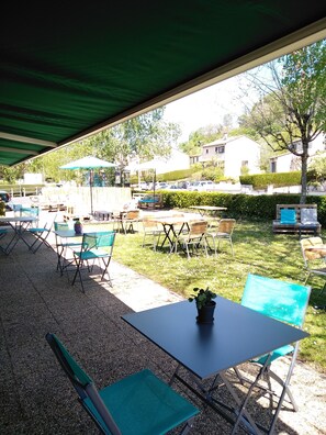 An outdoor patio area with tables and chairs, a covered seating area, and a view of residential buildings and parked cars. - Hotel Campanile Aurillac (Aurillac)