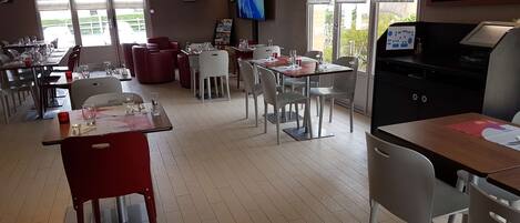 A restaurant with tables and chairs, a TV screen, and a menu board.