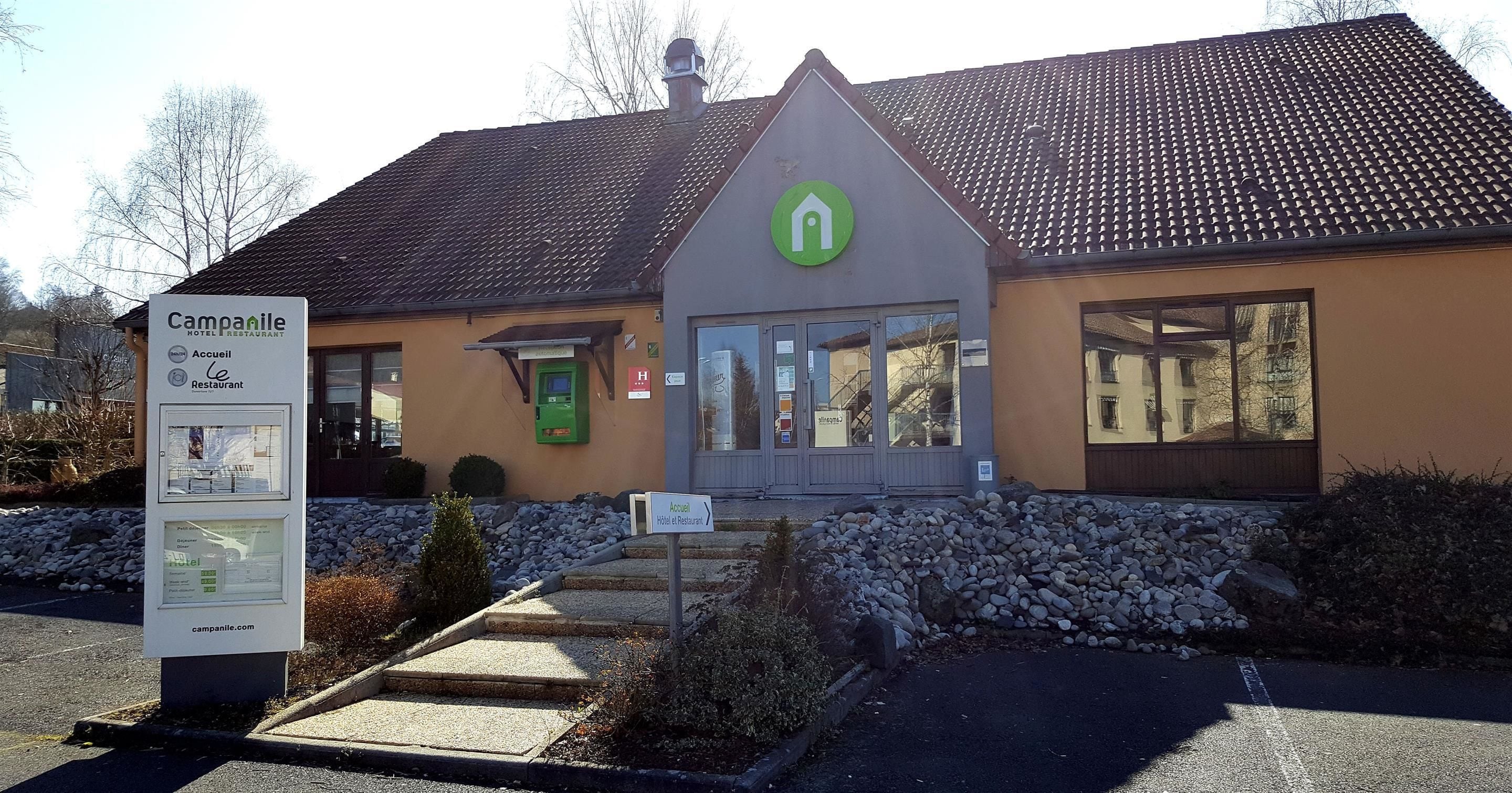 A hotel with a green logo, a reception desk, and a parking area.